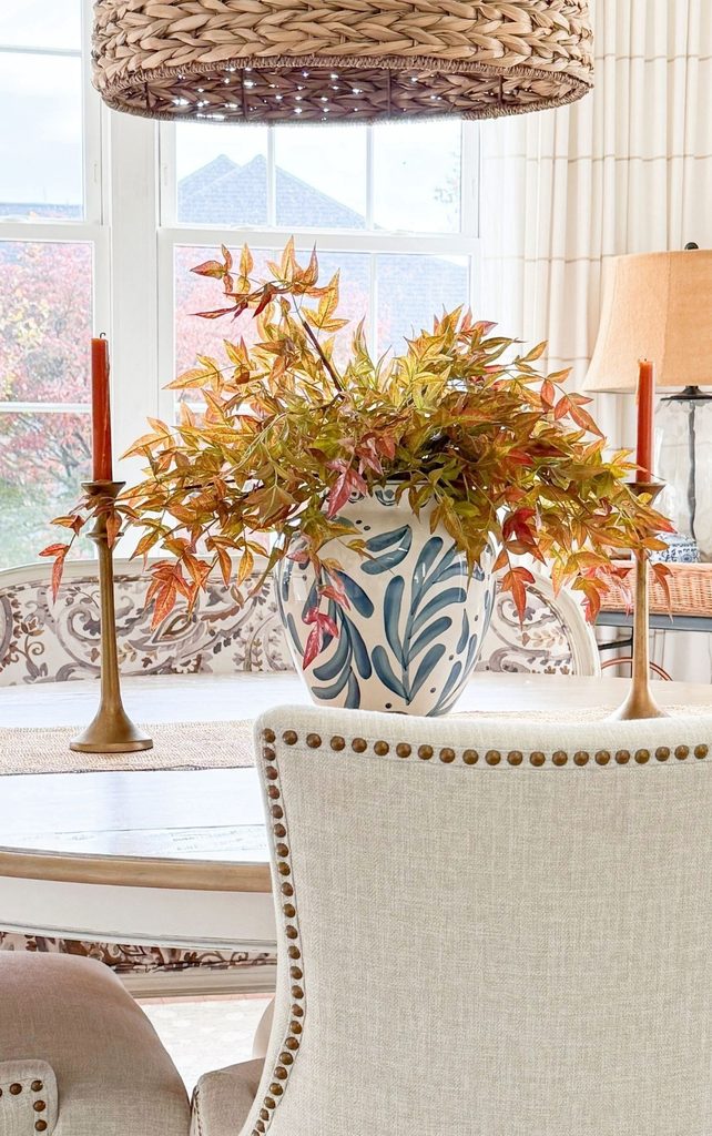 Fall branches in a blue and white vase between brass candlesticks with rust taper candles on a round breakfast table, bringing nature indoors for a Sunday Home