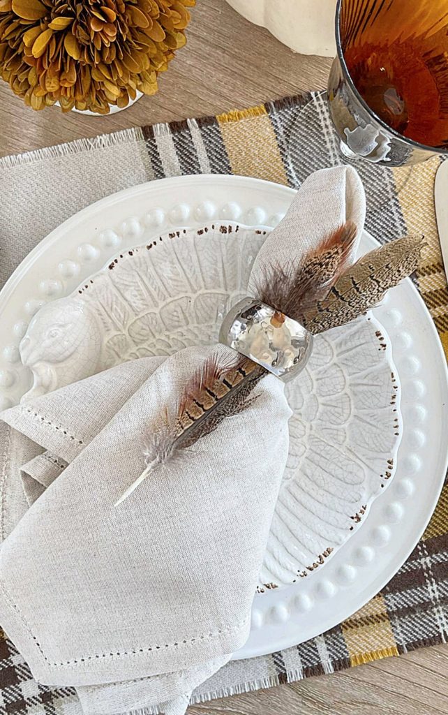 pheasant feathers tucked into a napkin ring on a Thanksgiving place setting