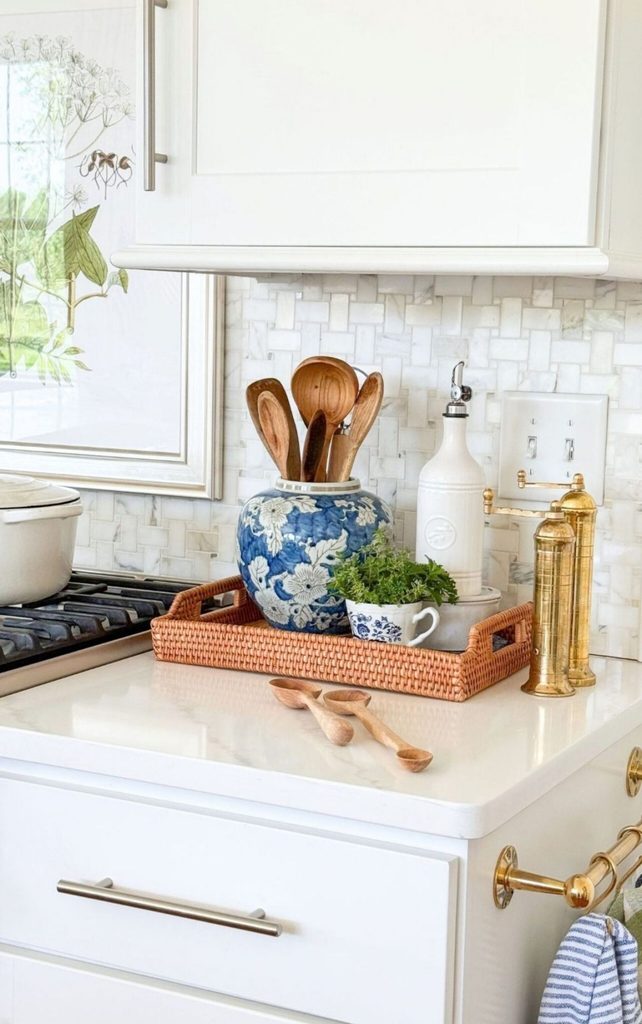 Kitchen counter by the stove with wooden spoons in a blue and white ginger jar, fresh herbs in a teacup, and brass pepper mills on a rattan tray, ready for simple Sunday Home meals
